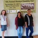 Photo of Kathleen, Lani, and Julie standing next to Disability Fair banner