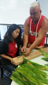 Photo of Tama teaching Krystaleia how to make ti leaf lei