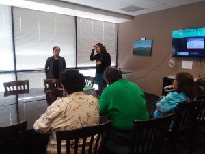 Photo of Raina talking to group, with interpreter standing next to her